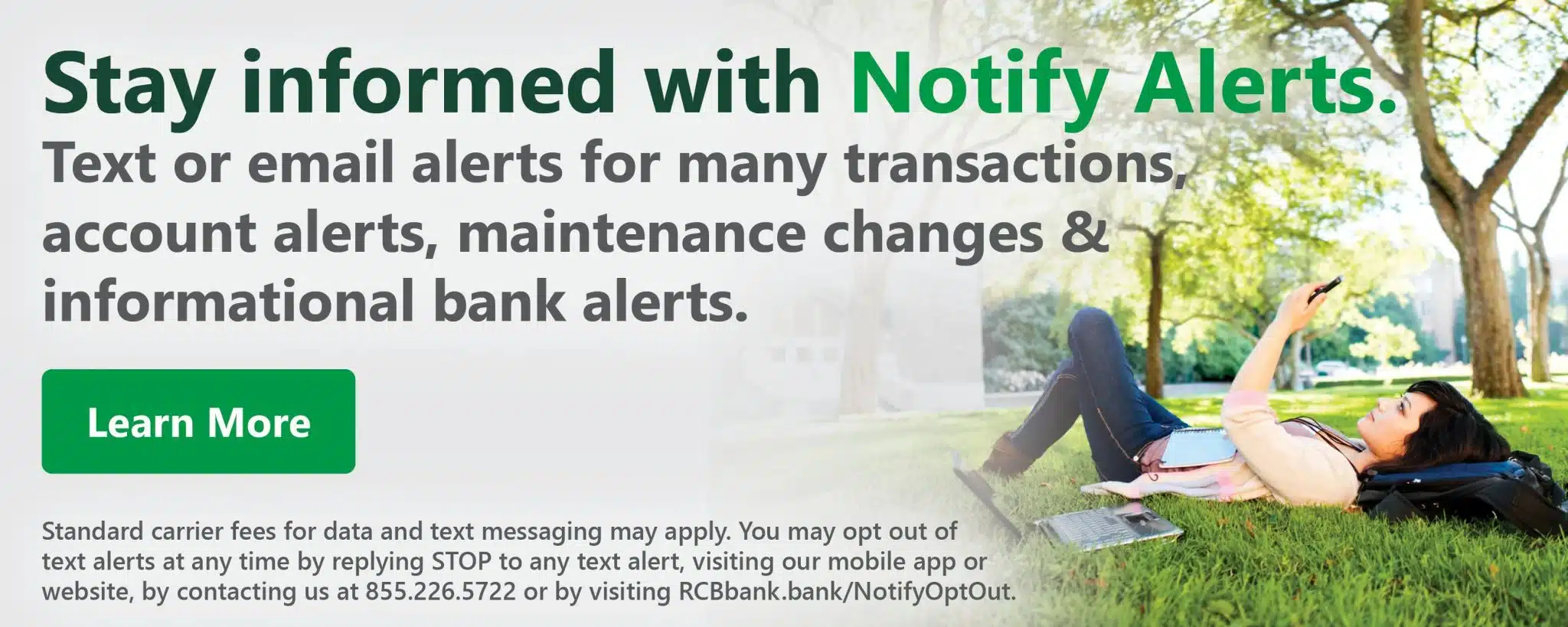 Woman relaxing on grass with a laptop and phone in a park. Text promotes "Notify Alerts" for bank transactions. Green "Learn More" button included.