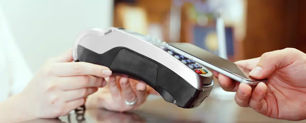 A person holds a smartphone near a card reader terminal to make a contactless payment.