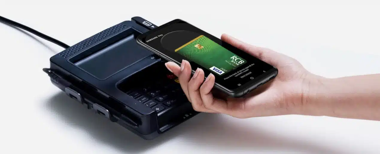 A hand holds a smartphone above a payment terminal, depicting a contactless transaction. The phone screen shows a digital credit card.